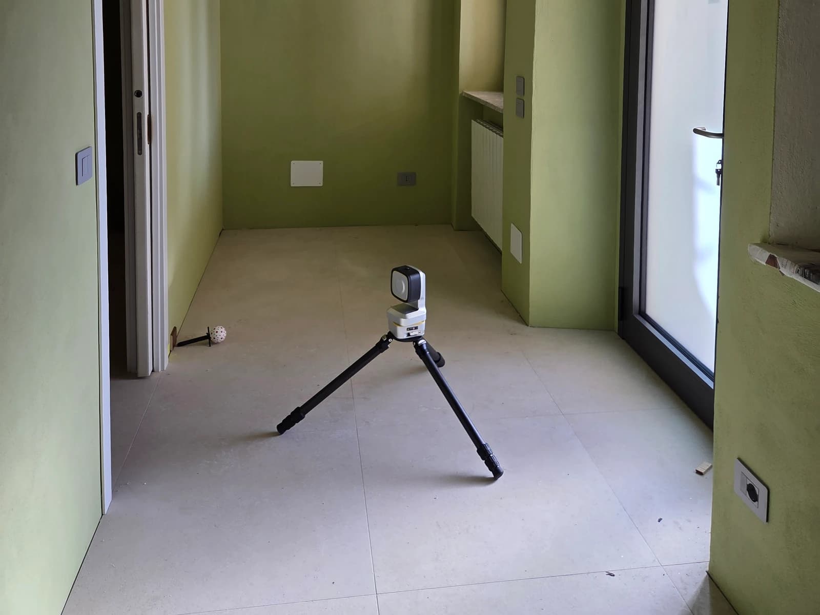 Misuratore laser robotico su treppiede durante il rilievo di un ingresso con pareti verdi, porte e rientranze